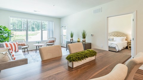 a living room with a table and chairs and a bedroom in the background